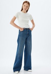 Hvid ribbet kortærmet top parret med højtaljede, brede blå denim jeans. Jeansene har et klassisk fem-lomme design og let blegning.