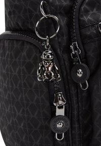 Black nylon backpack featuring a diamond pattern, silver hardware, and a monkey keychain accessory attached to the zipper pull.