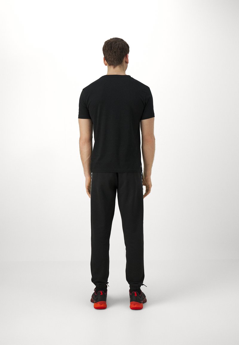 Czarny t-shirt z krótkim rękawem w połączeniu z czarnymi spodniami dresowymi. Strój charakteryzuje się prostym wzornictwem i luźnym krojem, uzupełniony butami z czerwoną podeszwą.