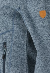 Grijze textuur fleece jack met een ritszak en een tan lederen logo patch. Heeft een casual en functioneel ontwerp.