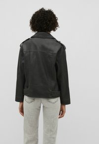 Veste en cuir noir avec épaulettes, col structuré et détails de couture visibles. Portée sur un jean taille haute gris clair.