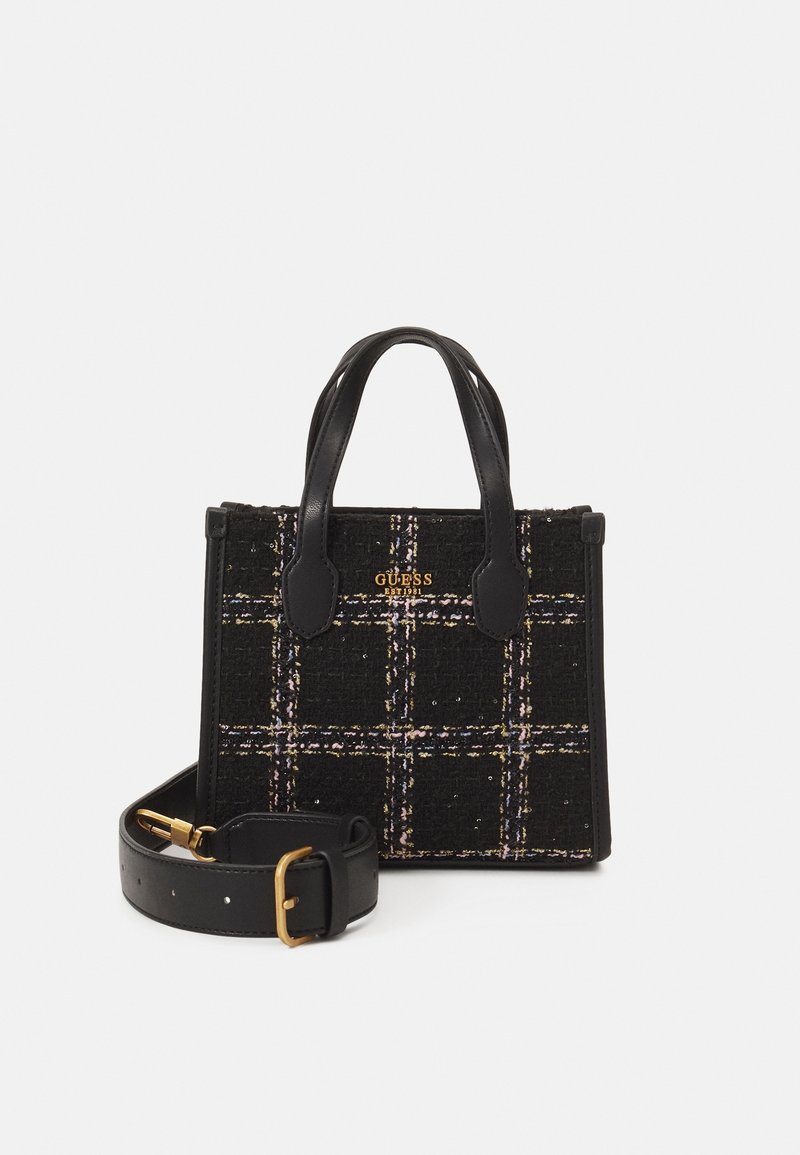 Petit sac à main noir en tissu à carreaux, double poignée, logo Guess doré et une bandoulière amovible en cuir noir avec une boucle dorée.