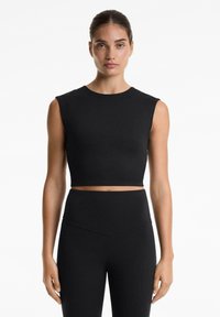 Top corto nero con maniche corte e scollatura rotonda, realizzato in tessuto elastico e liscio, abbinato a leggings neri a vita alta.