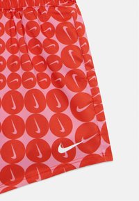 Pantalones cortos rojos con un fondo rosa, presentando un patrón repetido de círculos rojos y un logo blanco de Nike en el dobladillo.