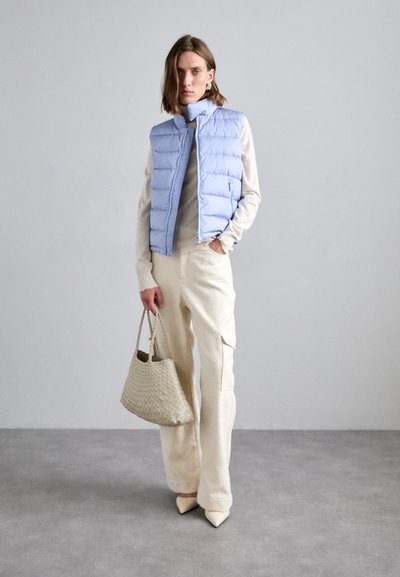 Hellblaues Puffer-Weste mit vertikaler Stepp-Textur, kombiniert mit einem cremfärbigen Pullover und off-white strukturierten Hosen. Beigefarbene, gewebte Handtasche und spitze Schuhe.