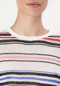 Gestreifter Strickoberteil mit roten, rosa, schwarzen und blauen Streifen auf weißem Hintergrund. Verfügt über einen Rundhalsausschnitt und gerippte Texture.