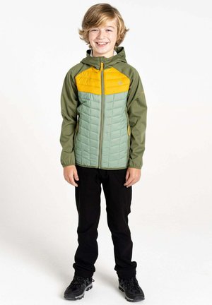 Grüne und gelbe gefütterte Jacke mit Reißverschluss, Kapuze und gestepptem Muster, kombiniert mit schwarzen Hosen und dunklen Schuhen.
