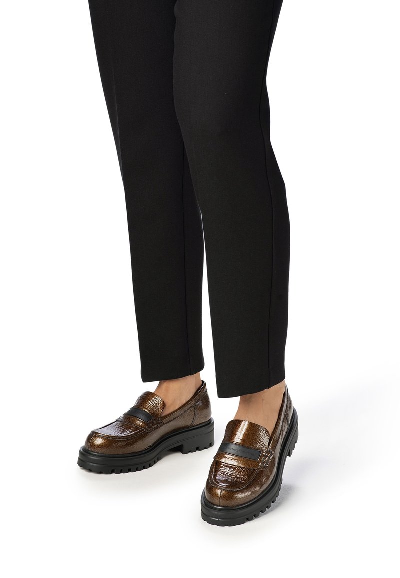 Mocassins en cuir marron avec une finition texturée et une semelle en caoutchouc noire. Présentent une large sangle sur le dessus pour un détail supplémentaire.