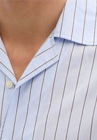 Camisa de rayas azul claro con finas líneas verticales. El cuello está doblado, con un cierre de botón visible en el cuello. Textura suave.
