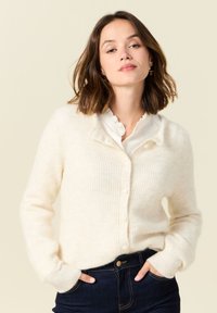 Kermainen ribbikuvioinen neulecardigan, jossa on pehmeä rakenne, napillinen etuosa ja rento malli, yhdistetty valkoiseen kauluspaitaan.