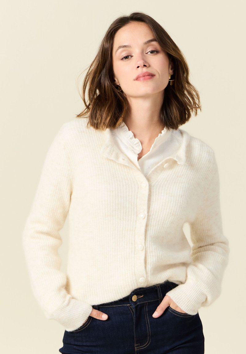 Kermainen ribbikuvioinen neulecardigan, jossa on pehmeä rakenne, napillinen etuosa ja rento malli, yhdistetty valkoiseen kauluspaitaan.