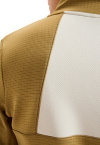 Bruine gestructureerde stof met een ruitpatroon, met een contrasterend witte sectie. Het ontwerp heeft een gladde, ademende textuur.