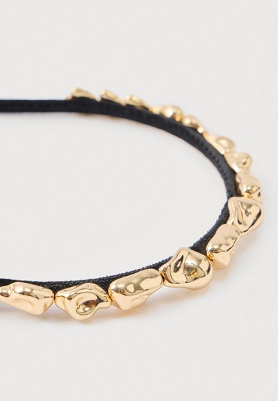 Czarna elastyczna gumka do włosów ozdobiona nieregularnymi, błyszczącymi złotymi metalowymi koralikami równomiernie rozmieszczonymi na całej długości, na białym tle.