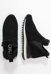 Bottes basses en daim noir avec un col en fausse fourrure, des panneaux latéraux élastiques, et une semelle compensée en caoutchouc texturée avec un détail de bande blanche.