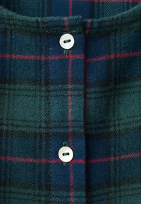 Tissu en flanelle à carreaux vert et bleu marine avec une texture douce, comportant des lignes rouges contrastantes, un bouton rond clair et un col.