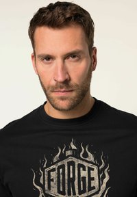 Sort bomulds T-shirt med et slidstærkt gråt grafisk print af ordet "FORGE" omgivet af flamemotiver i en hexagonal form.