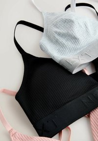 Trois bralettes côtelées : noir avec bretelles noires, bleu clair avec bretelles grises, et rose avec bretelles roses. Toutes disposent d'une bande élastique distincte.