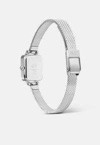 Montre en acier inoxydable argenté avec un boîtier carré, un bracelet en maille et une fermeture sécurisée. Le dos affiche les détails du fabricant et les informations sur le mouvement.
