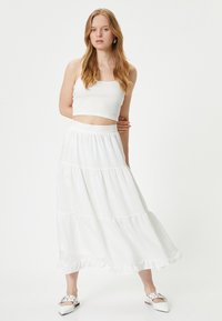 Top corto blanco sin mangas combinado con una falda maxi blanca de capas, fluida, que presenta detalles con volantes y una cómoda cinturilla elástica.