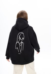Felpa nera con cappuccio e un grande disegno a linea bianca sul retro, caratterizzato da un design minimalista di un volto. Tessuto morbido e vestibilità rilassata.