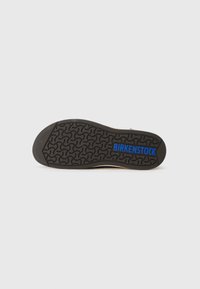 Black rubber shoe sole with textured pattern, featuring a blue "BIRKENSTOCK" logo. Light-colored footbed edges visible around the sole.