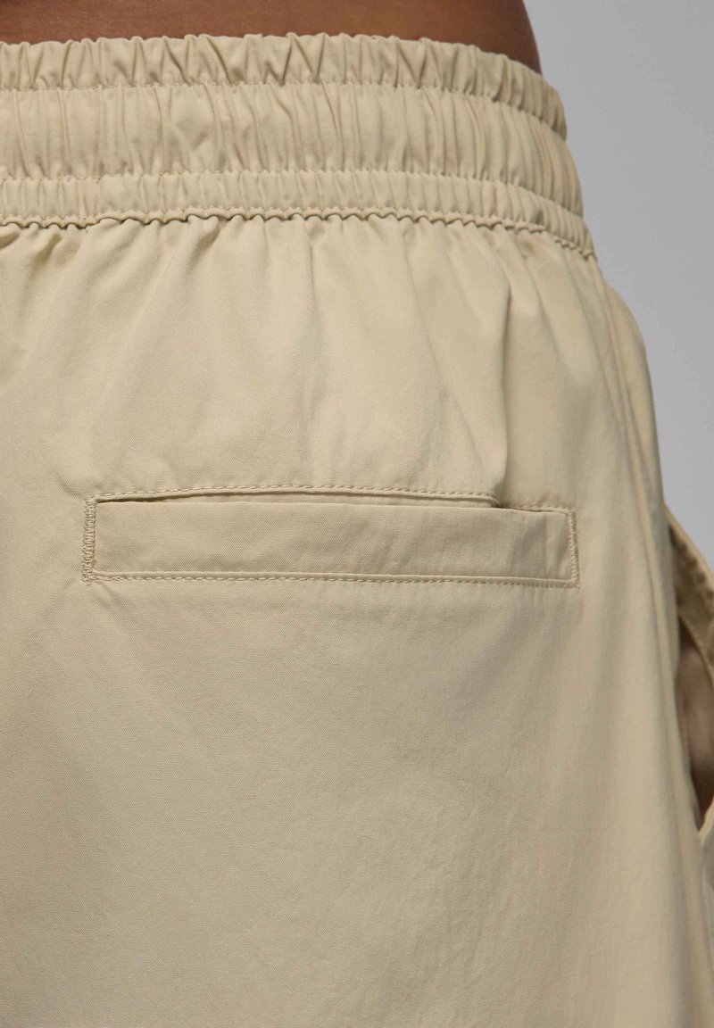 Shorts beiges avec une ceinture élastique et une poche arrière plate. Tissu lisse et léger avec une texture subtile. Détails de conception ajustés.