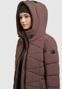 Mauve'ist vooderiga jakk kõrge kraega ja suure kapuutsiga, millel on diagonaalne õmblemine, must tõmblukk ja logoplekk varrukal.