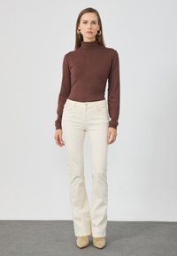 Brūns turtlenecks džemperis, krēmkrāsas flared bikses. Džemperim ir garas piedurknes; biksēm ir priekšējās kabatas un pogu aizdare. Gaisīga, mīksta auduma.