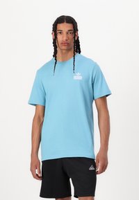Gaiši zils kokvilnas t-krekls ar īsām piedurknēm, kuram uz kreisā krūškurvja ir neliels balts Adidas logo prints. Apvienots ar melniem šortiem.