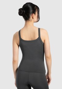 Canotta grigia aderente con spalline sottili, tessuto texture e design a scollo lungo, abbinata a pantaloni da allenamento coordinati. Nessun logo visibile.