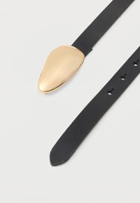 Mustast nahast rihmaga kell, millel on läikiv kuldse tooniga pisarakuju sihverplaat. Rihmal on mitmed reguleerimisaasad, sile tekstuur ja elegantne disain.