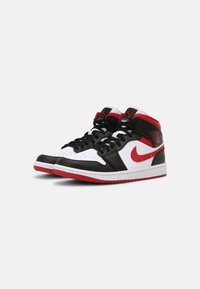 Pár černých, bílých a červených vysokých tenisek s černými šňůrkami, červeným Nike swoosh a červenou podrážkou na jednobarevném pozadí.