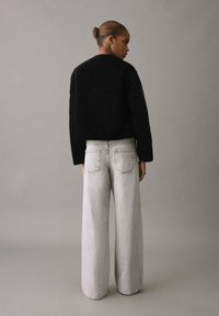Suéter negro de punto trenzado corto con mangas largas, combinado con jeans de pierna ancha gris claro que presentan un diseño clásico de cinco bolsillos.
