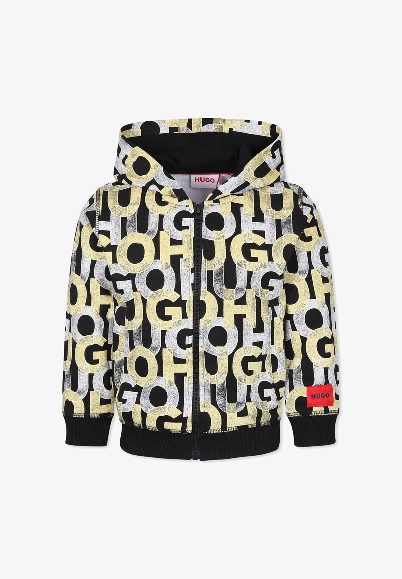 Sweat à capuche zippé noir, avec de grandes lettres graphiques jaunes et blanches. Étiquette rouge "HUGO" sur le devant. Texture douce, poignets côtelés.