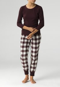 Bordowa bluzka z długim rękawem w połączeniu z białymi i ciemno-bordowymi w kratkę spodniami piżamowymi. Spodnie mają elastyczne mankiety i luźny krój.