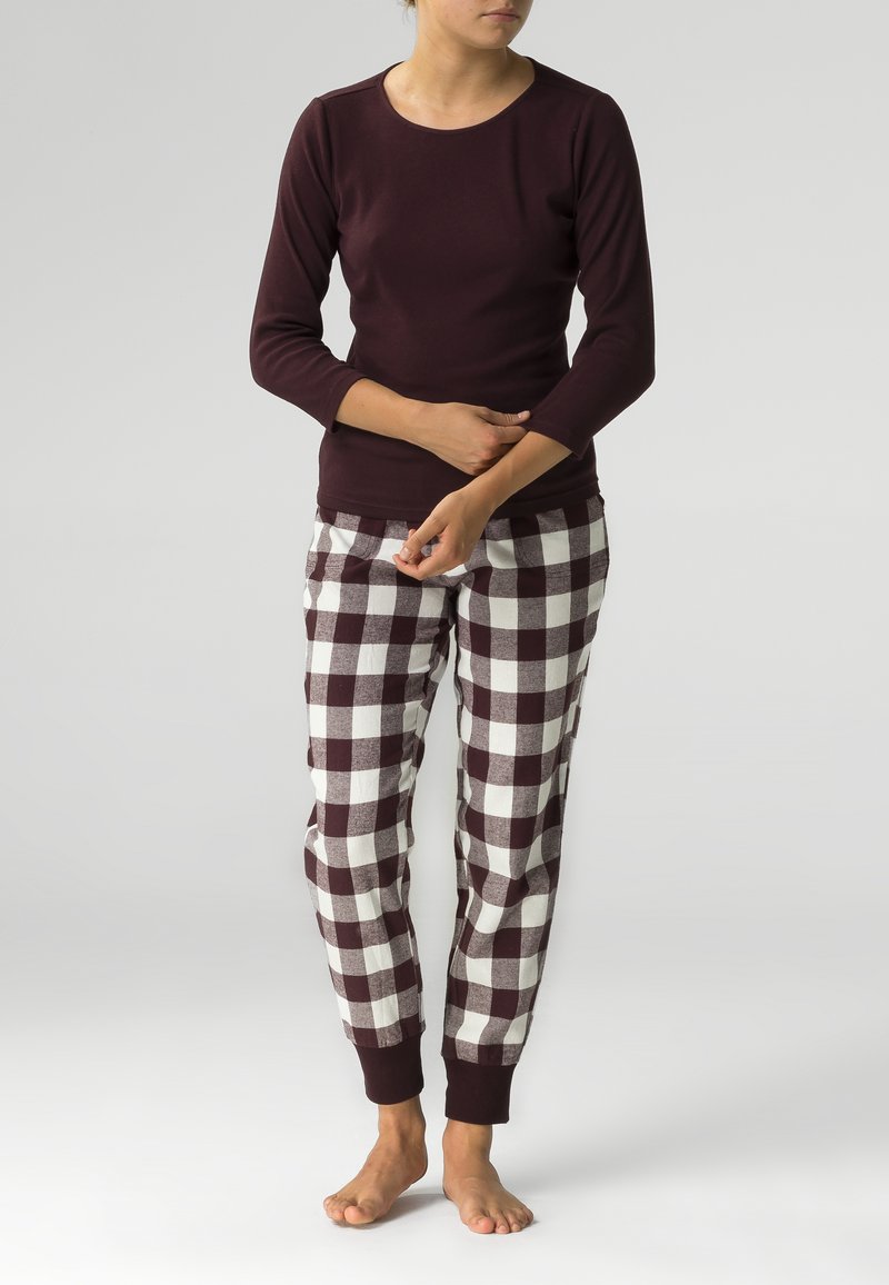 Bordowa bluzka z długim rękawem w połączeniu z białymi i ciemno-bordowymi w kratkę spodniami piżamowymi. Spodnie mają elastyczne mankiety i luźny krój.
