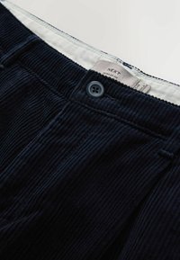 Dark navy corduroy trousers with a textured surface, featuring a button closure and a white inner waistband label displaying brand and size.