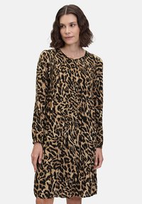 Robe à imprimé léopard avec des manches longues, un col rond et un détail froncé à l'avant. Fond noir avec des motifs beiges et marron. Texture de tissu douce.