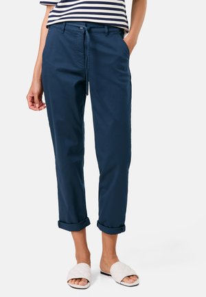 Dunkelblaue Baumwollhose mit umgeschlagenem Saum, Kordelzugbund und Seitentaschen, kombiniert mit weißen, gesteppten Slidesandalen.