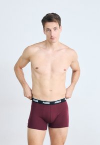 Boxeri maroon dintr-un material moale, cu un brâu elastic negru pe care se află logo-ul "PUMA", concepuți pentru confort și ajustare.