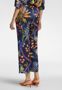 Pantaloni a gamba larga blu scuro con motivo floreale e colori vivaci. Tessuto liscio, vita elastica e tacchi arancioni a contrasto.