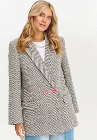 Dvojřadový blazer v houndstooth vzoru s barevnými tečkami. Má růžové knoflíky, boční kapsy a uvolněný střih.
