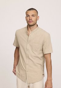 Chemise à manches courtes en khaki en tissu léger avec une fermeture à boutons, col rond, poche poitrine et détails de texture subtils.