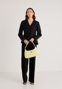 Čierna ľanová bunda na gombíky, v kombinácii s čiernymi nohavicami a žltou koženou kabelkou s guľatým tvarom a kovovým zdobením.