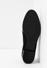 Chaussure en suède noire avec une semelle noire lisse, présentant un design effilé. Dispose d'un petit talon et de texte en relief sous le pied. Taille 37.