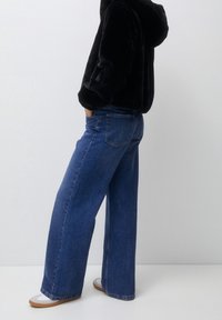 Szerokie niebieskie dżinsy z średnim przepierzeniem, z pięcioma kieszeniami i luźnym krojem, zestawione z czarną polarową bluzą z kapturem.