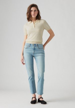Polo shirt jaune clair avec un col côtelé et des manches courtes, associé à un jean tapered bleu clair et des chaussures plates noires.