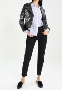 Černá kožená motorkářská bunda s květinovou výšivkou, světle modrá košile s límečkem, černé džíny a černé pantofle s kožešinovými akcenty.