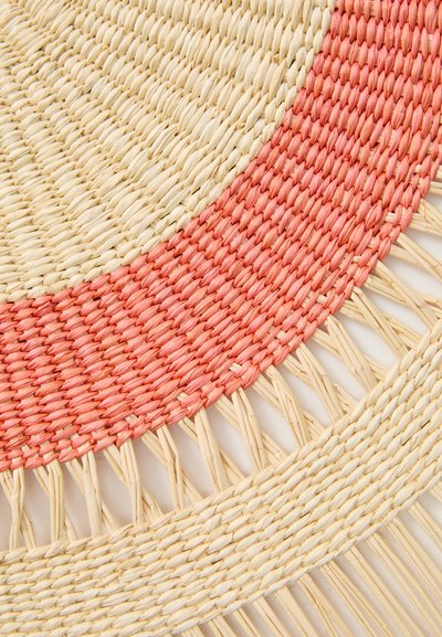 Round woven mat with beige and coral sections, featuring a textured straw finish and intricate braid details around the edges.