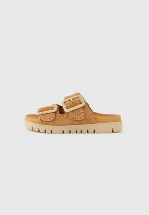 Tan suede slide sandal with two large buckles, stitched detailing, and a thick, textured sole featuring a zigzag pattern.